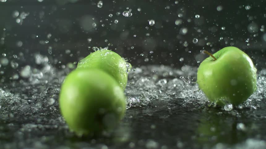 A large amount of water is dumped on granny smith apples in a studio
