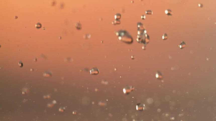 Crystalline drops of water fall and splash creating a spray against an orange brown background