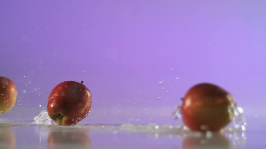 Apples are rolling in water and splashing drops of water into the air
