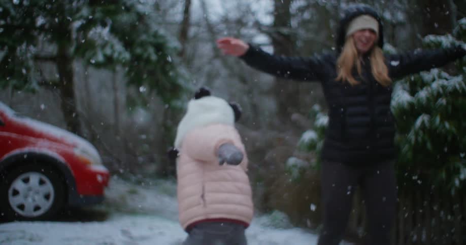 Mother and daughter are playing outdoors as snow falls