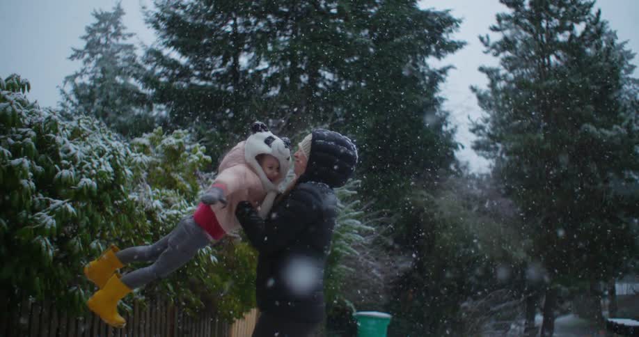 A woman swinging her child around outdoors on a snowy day