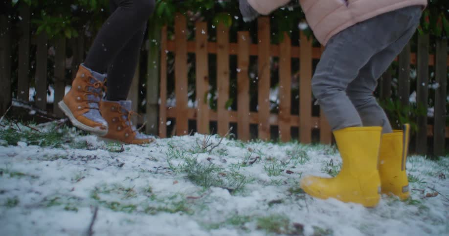 A people wearing winter boots jump and play on the snow covered grass amidst a light snowfall