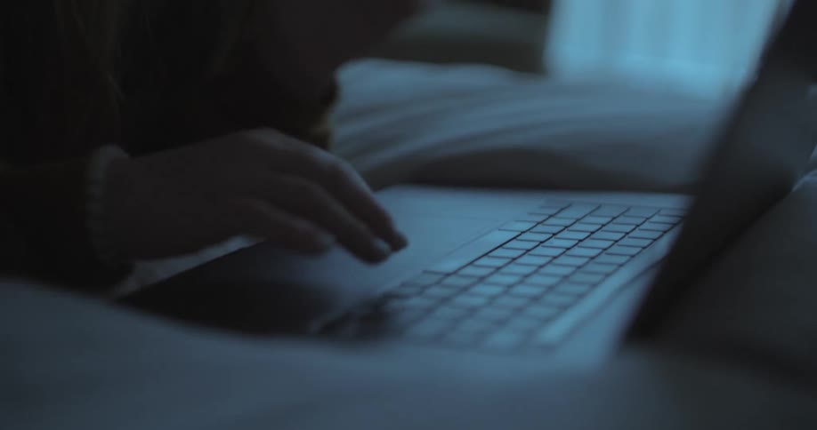 A woman is typing on her laptop in bed