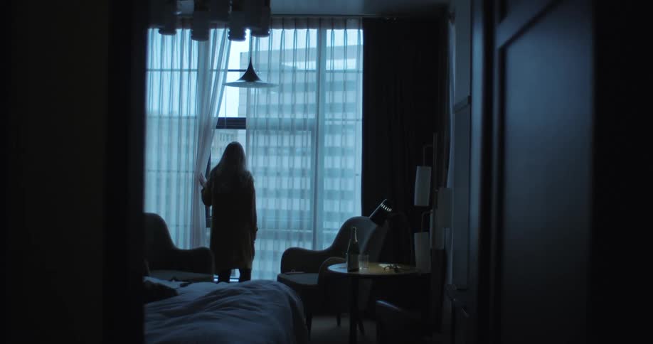 A woman stands at a large hotel room window looking out