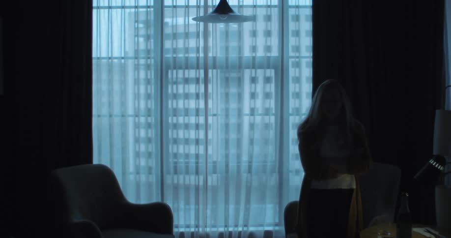 A woman is pacing back and forth in front of a window
