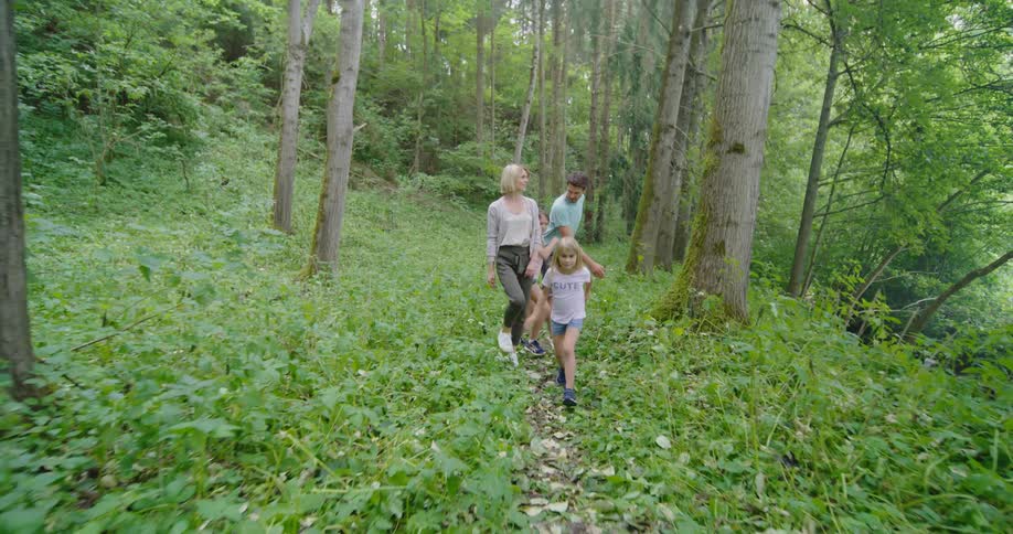 Mother and father with daughters walk along track in the woods