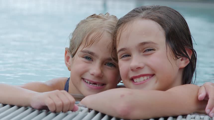 Two young girls in a swimming pool pause to pose together and smile for the camera