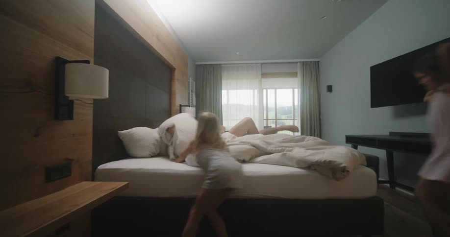 Two girls run into the bedroom and hit their parents with pillows