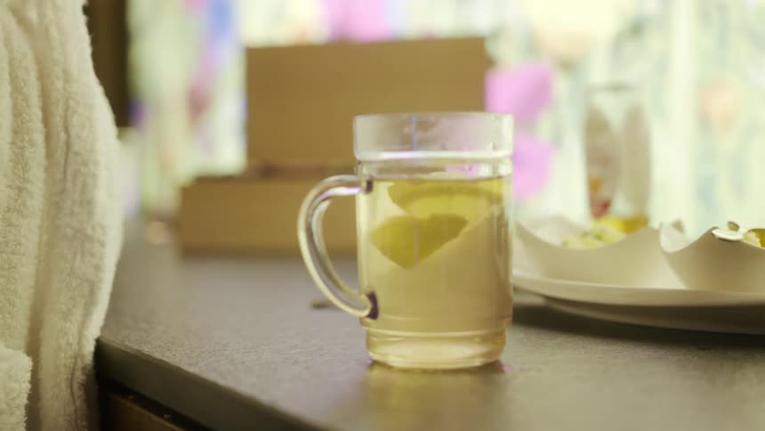 Woman with white bathrobe puts lemon piece into a glass of tea with fork