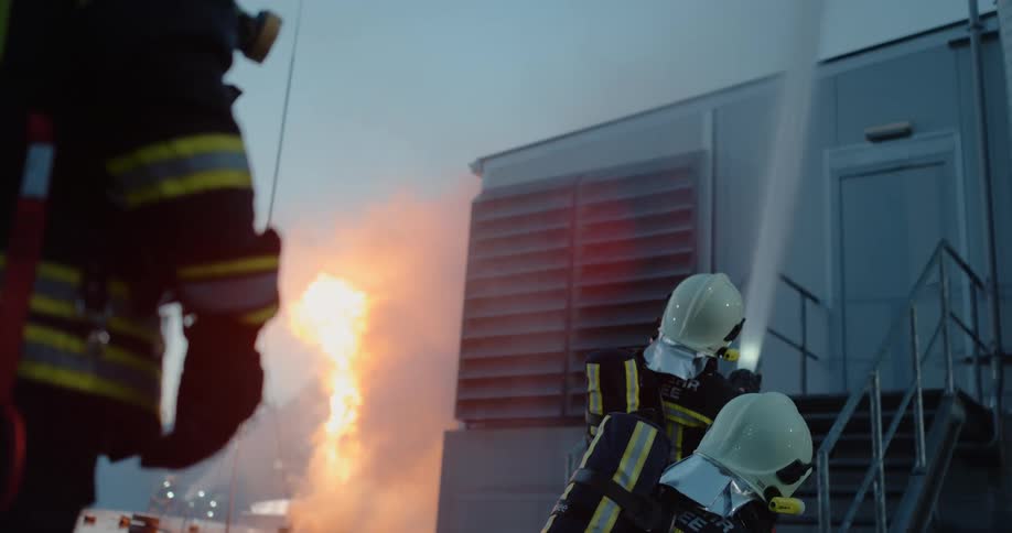 Firefighters and battling a fire as one fireman holds a hose spraying water on a building
