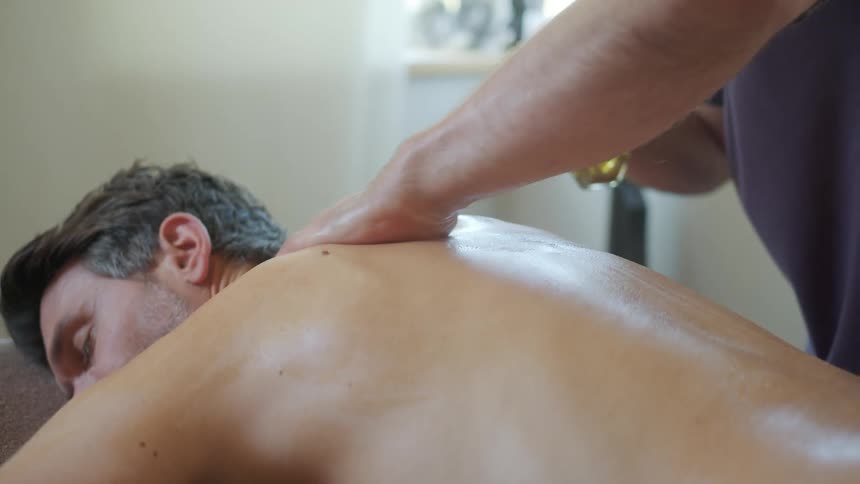 A man is laying on a table as someone is rubbing oil on his back