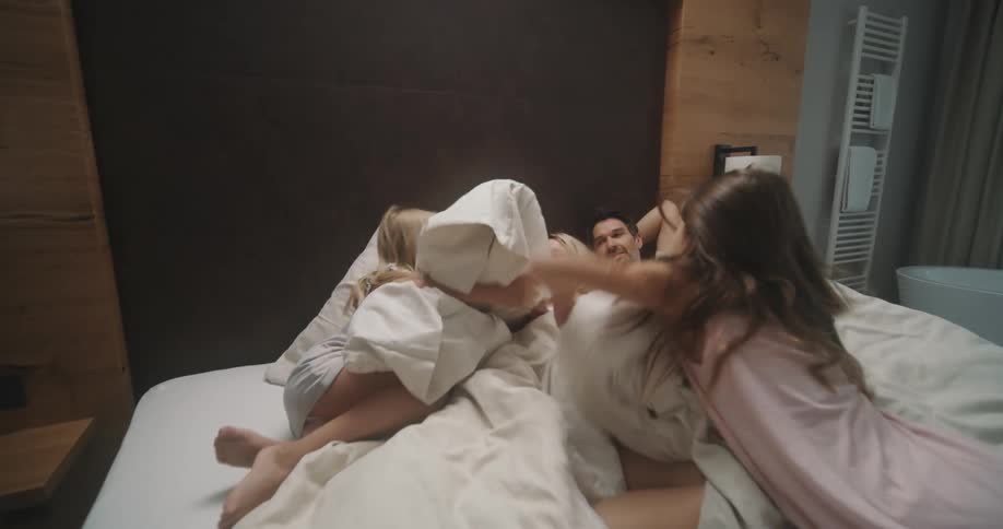 Two girls jump into a hotel bed to join their parents
