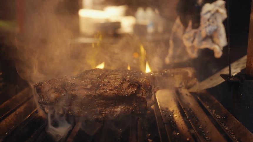 A person with gloves cooking meat on a grill with fire and smoke