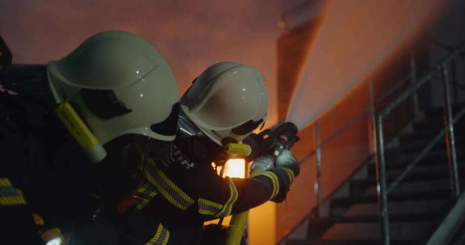 Firefighters have a hose pointed at a fire in a building