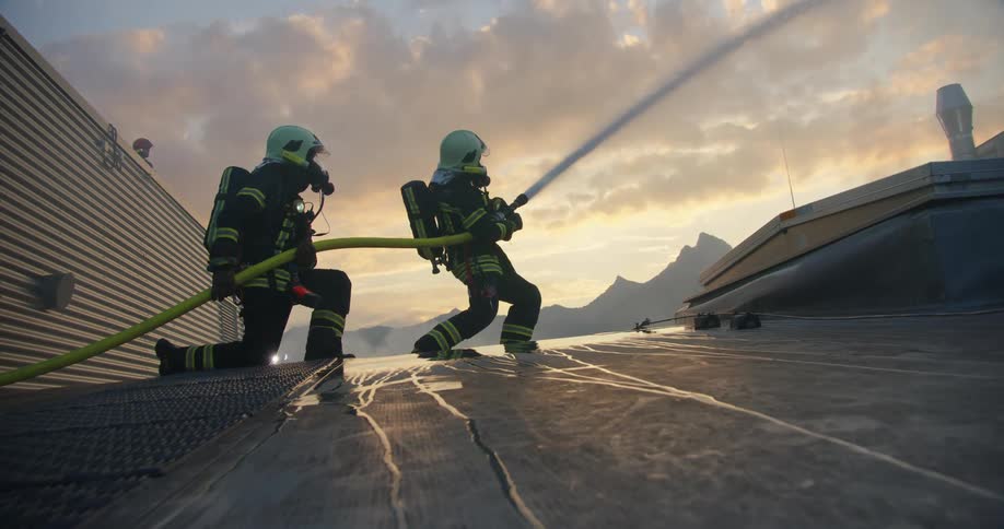 Two firefighters using a hose to spray water