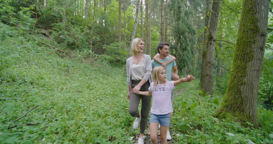 Family of four leisurely walking on a trail through the forest at daytime