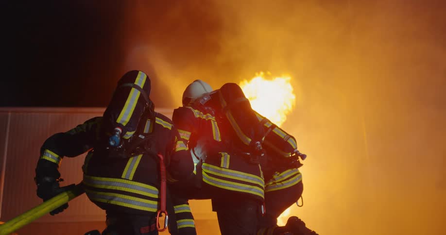 Three firefighters are fighting a fire at night