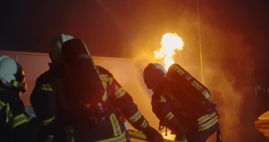 Firefighters use a hose to fight a flaming smoky fire at night