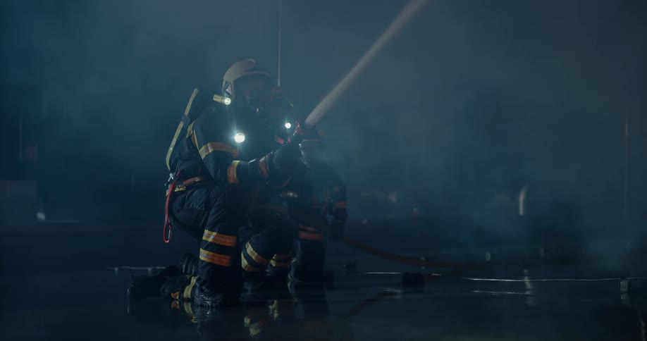 A firefighter uses a hose to spray a fire as smoke floats in the air