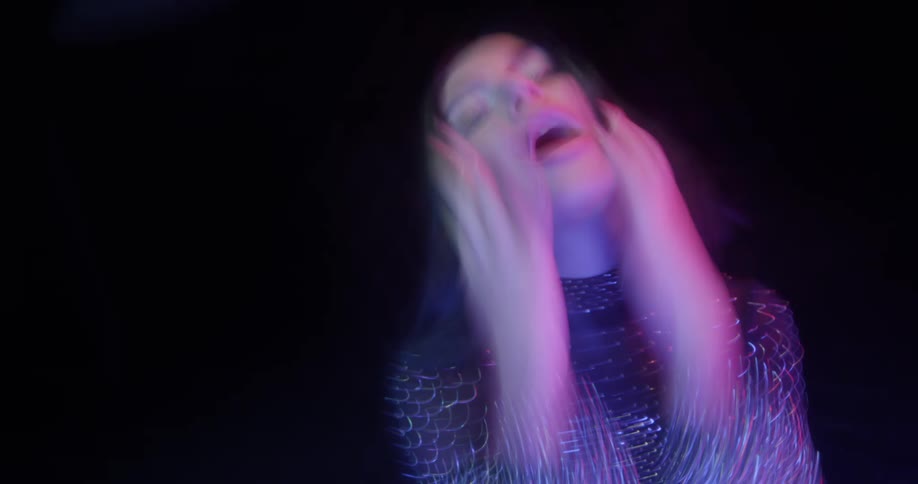 A woman wearing a sparkly leotard dances proactively with colorful lights glowing