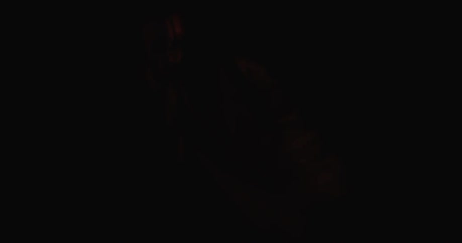 A young girl in a halloween mask stands in a dark room