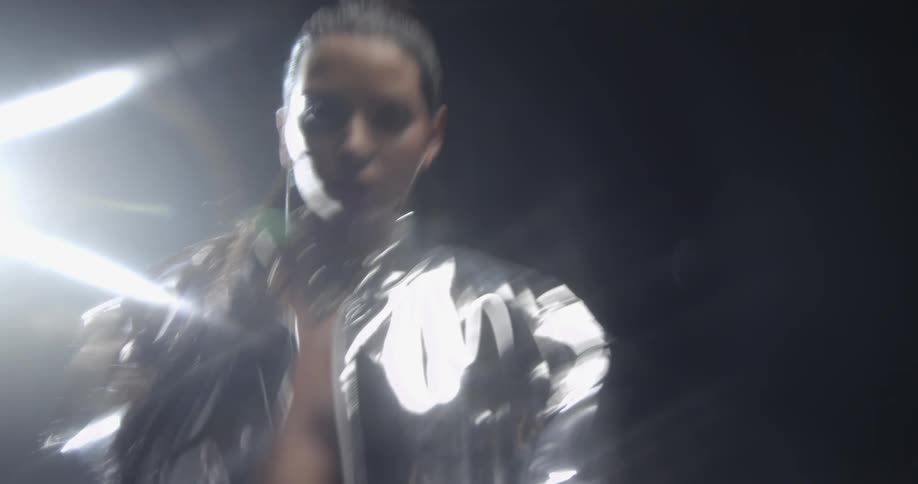 A woman wearing a silver outfit with earrings in a room with lights in the background