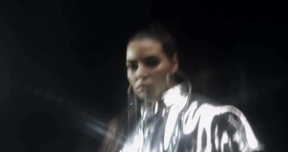 A woman wearing a silver outfit with earrings in a room with lights in the background