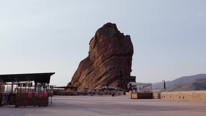 Open air sitting areas fill plaza leading to tall rock outcropping with hills background