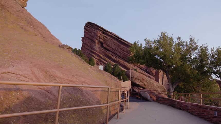 A pathway with railing with trees a cliff the sky and clouds in the background