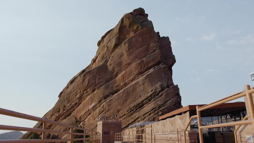 Large narrow stone mountain rises above covered open air buildings and railed bond walkway