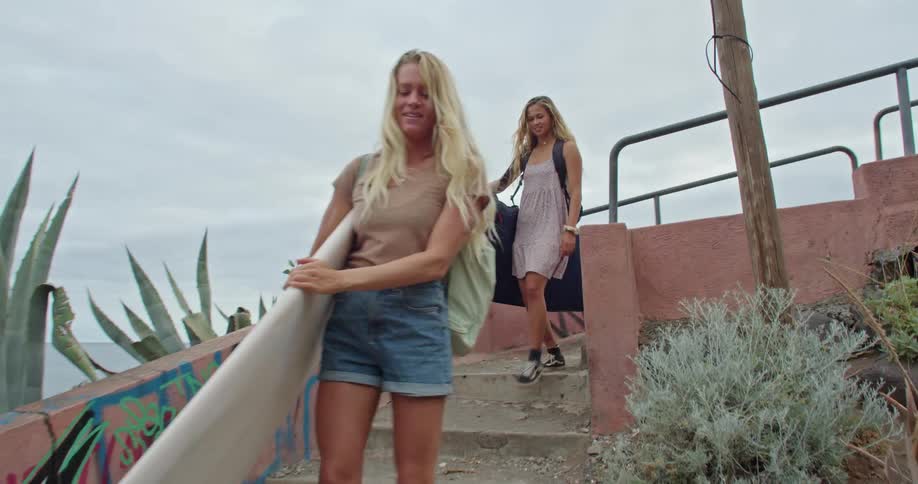 Two women walking down stairs carrying surfboards