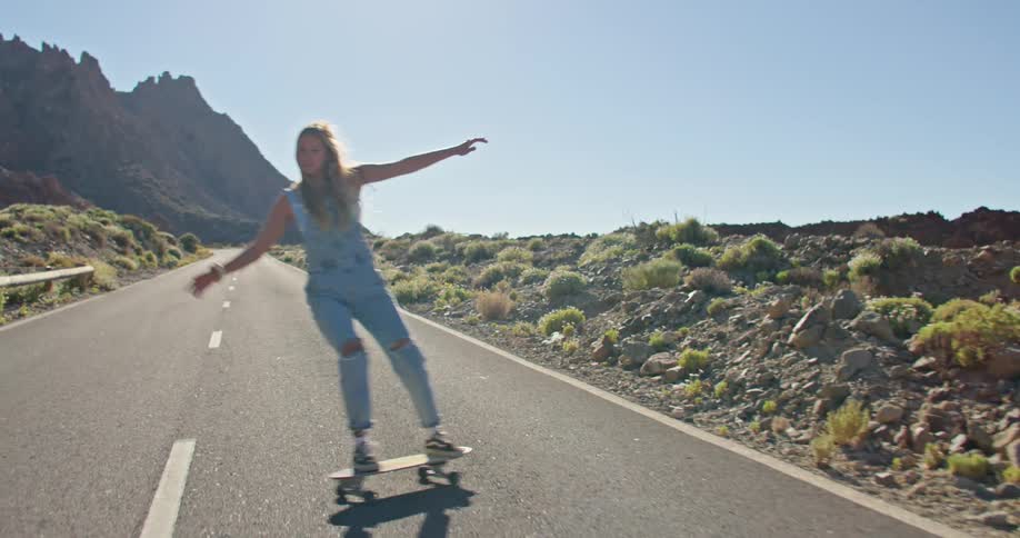 A woman rides a skateboard on an empty road through the desert on a bright sunny day