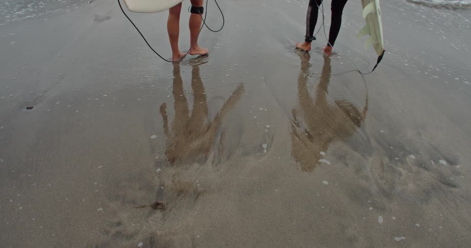Two men holding surfboards are on the beach facing the water