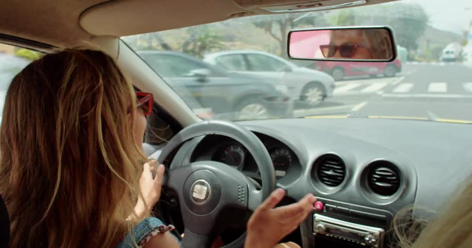 Two girls are in a car driving down the road and the driver runs a stop sign