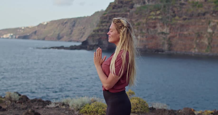 A woman standing near a coast with water a cliff the sky and clouds in the background