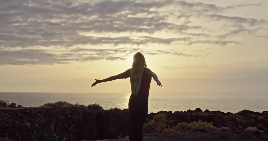 A woman is looking over a body of water as she does yoga