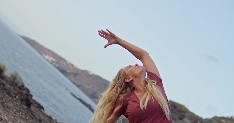 A woman stretching near a coast with the ocean sky and clouds in the background