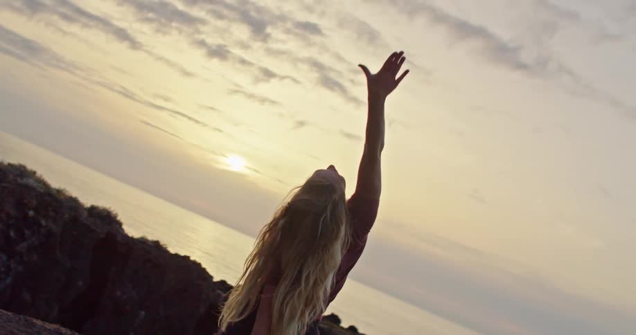 Blonde woman moves through yoga poses facing sun and ocean on horizon