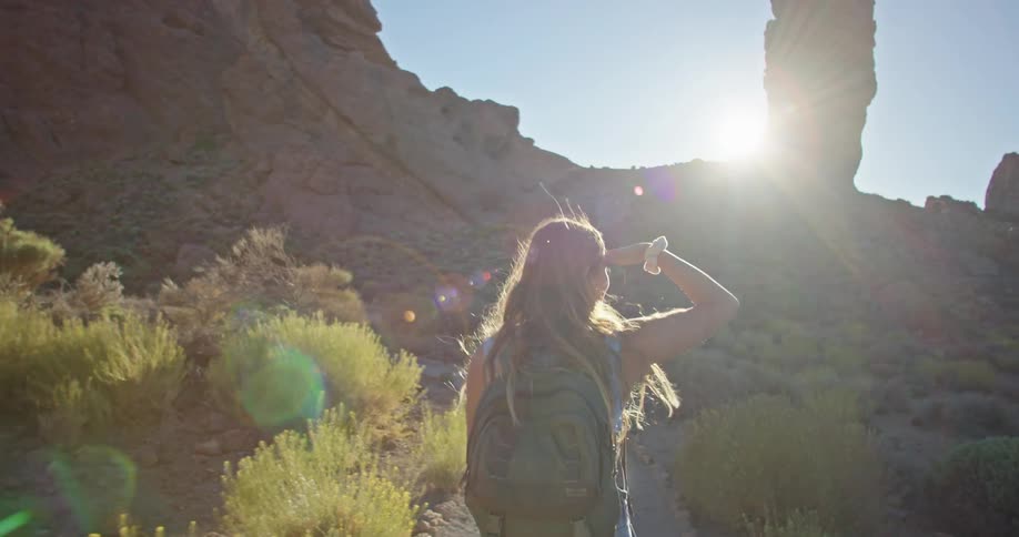 A woman shields the sun with her hand as she hikes through a canyon