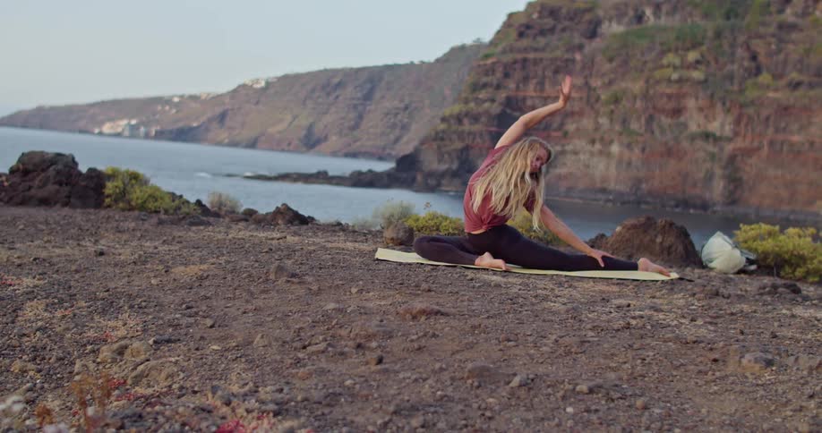A woman with long blond hair is doing yoga exercise on a mat next to a mountain river