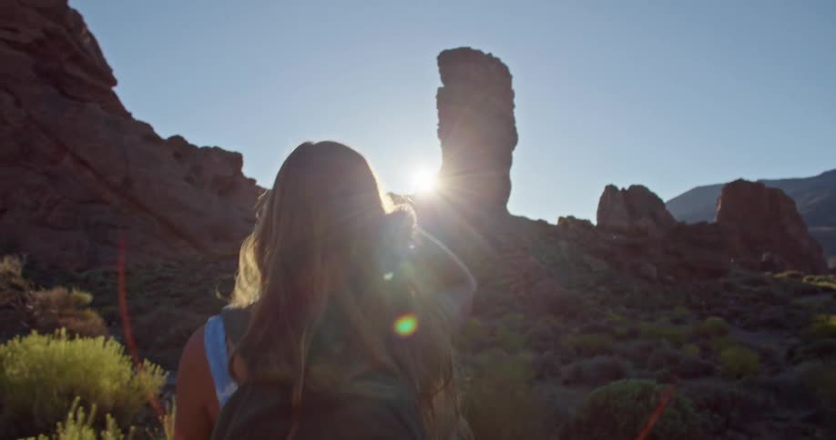 A woman shields her eyes from the sun as she hikes in the mountains