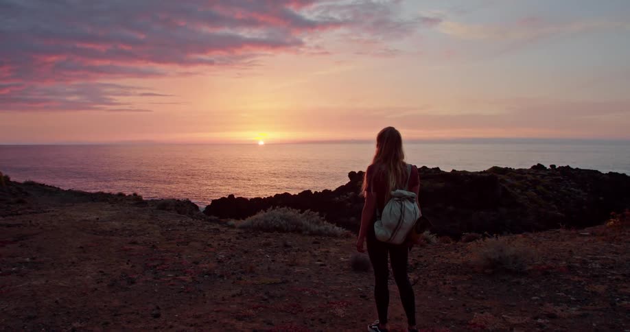 A teenage girl walks along the shore carrying a yoga mat as the sun sets