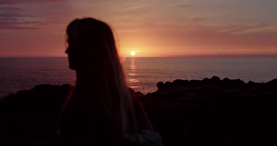 A woman walks along the coast at dusk