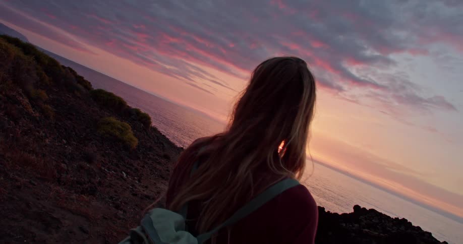 A woman with a backpack near a coast with the ocean the sky and clouds in the background