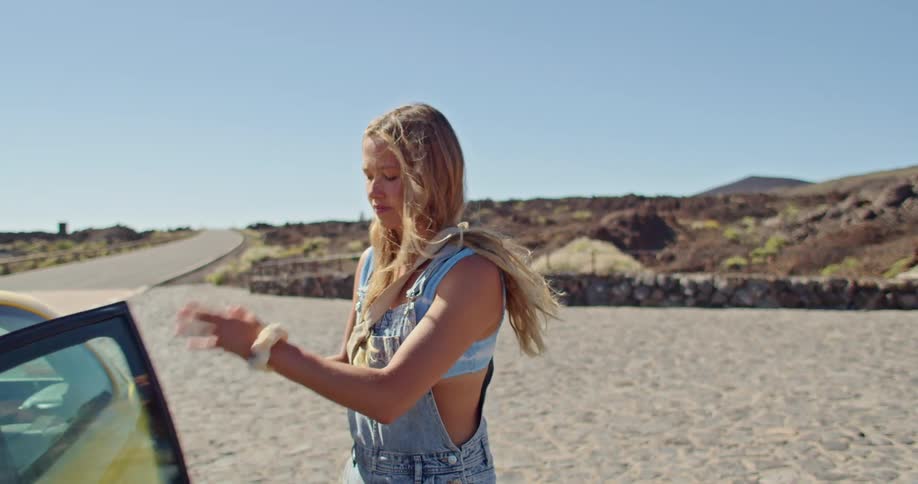 A blonde woman closes her car door and picks up a skateboard