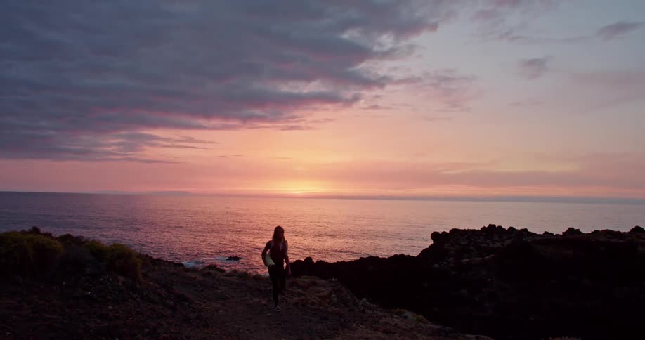 Woman leaving the cliff is silhouetted against the sea and sunset