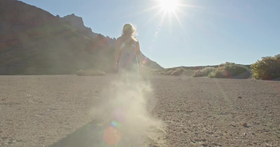 A woman drags a branch in soil while walking through the desert