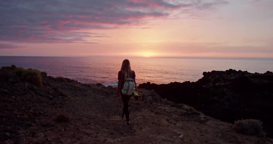 A woman hiking along a cliff at sunset