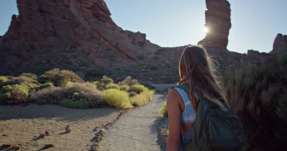A woman walks on a marked trail in the desert looking up at the glaring sun