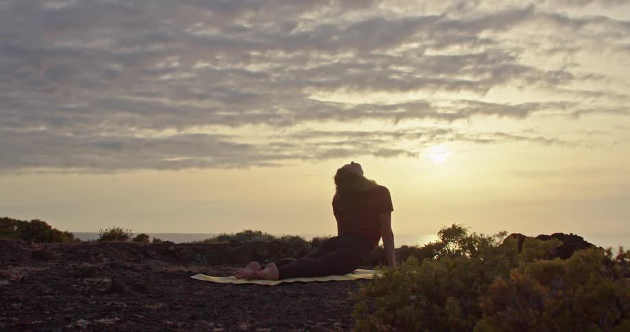 A woman stretches while doing yoga on a cliff at sunrise